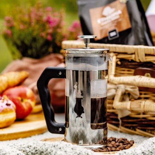 french press naplnený kávou a v pozadí piknikový košík