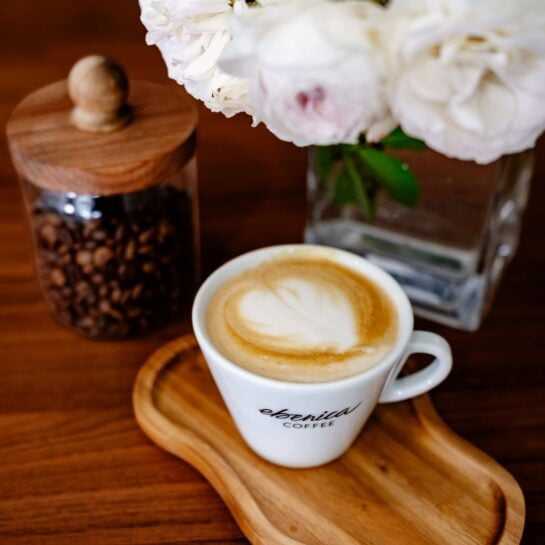 cappuccino v šálke EBENICA COFFEE na stole s kvetmi